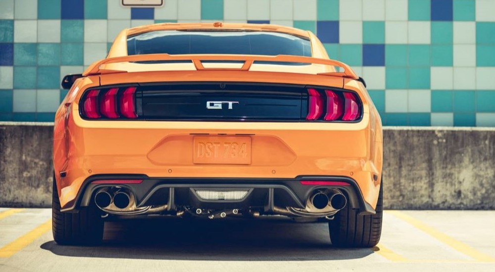 Seen from the rear, an orange 2018 Ford Mustang GT is parked in front of a tile wall.