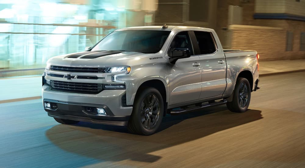 A silver 2020 Chevy Silverado 1500 RST Rally driving on a well-lit city street at night.