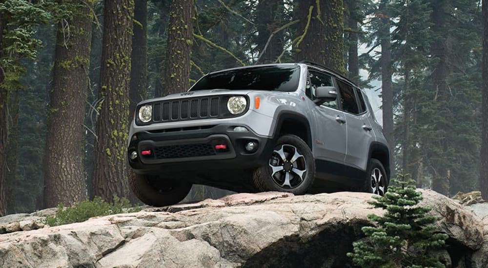 A silver 2019 Jeep Renegade driving over large boulders while off-roading in the woods.