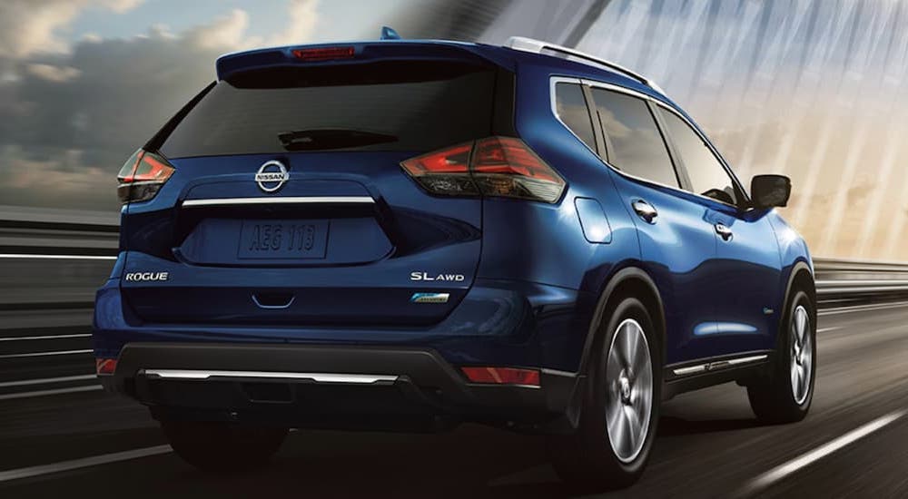 A blue 2017 Nissan Rogue SL is shown from the rear while driving on a large bridge.
