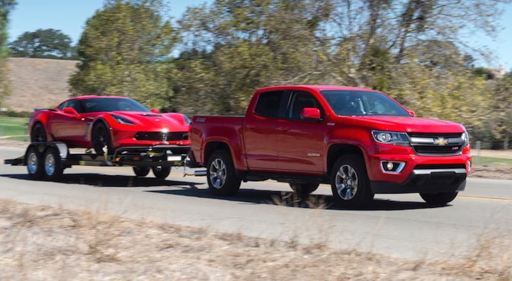 A red 2018 Chevy Colorado towing a red Corvette on a trailer.