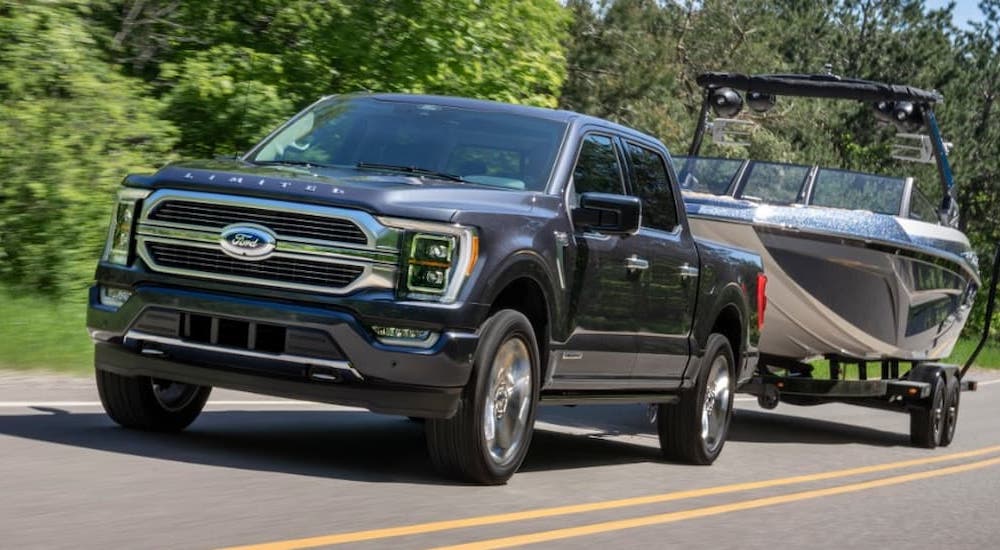 A black 2021 Ford F-150 Hybrid Limited towing a boat on an open road.