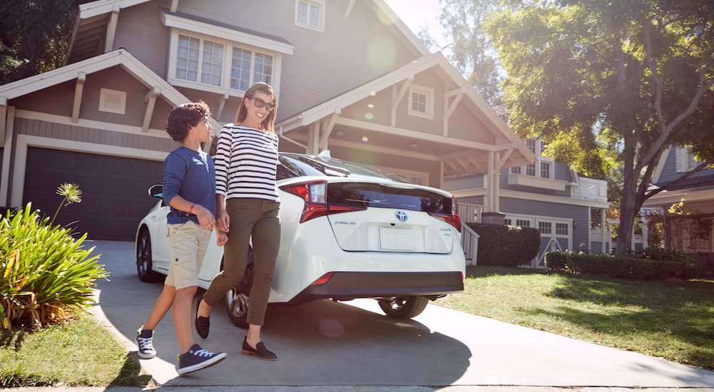 A mother and son walking past a white 2021 Toyota Prius parked in their suburban driveway.
