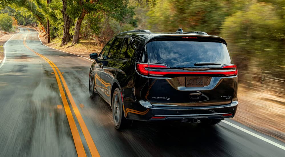 Rear view of a navy blue 2021 Chrysler Pacifica driving on a country road.