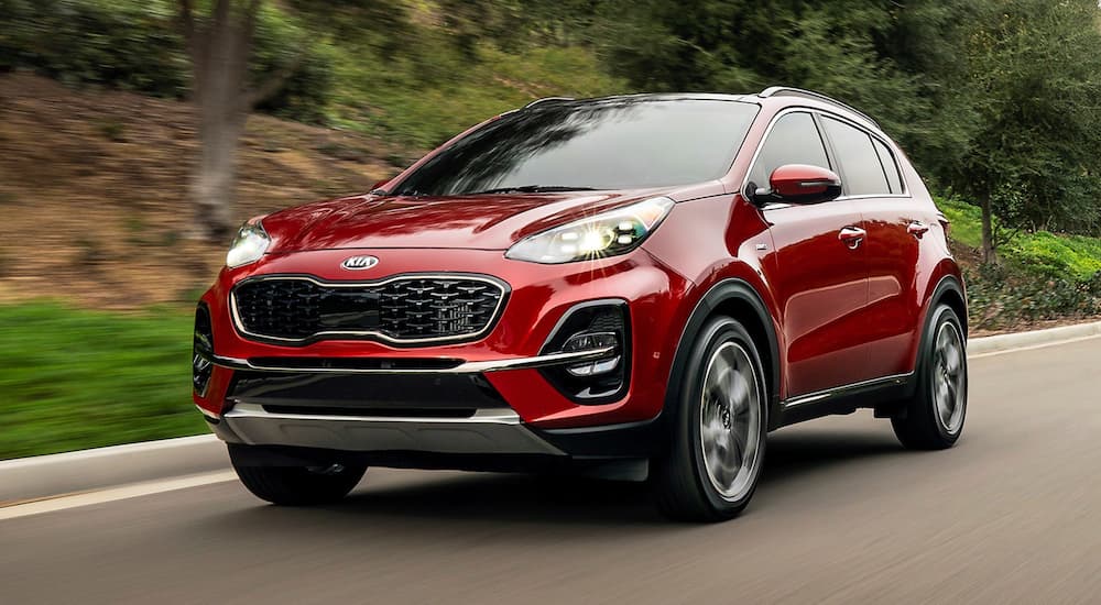 A red 2020 Kia Sportage driving on a tree-lined road.