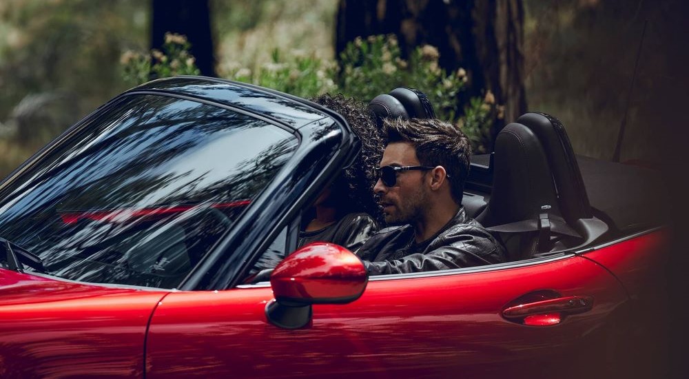 A man with sunglasses driving a red 2019 Mazda MX-5 Miata with the roof down.